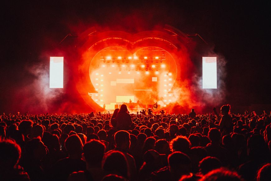 crowd in front of a stage shaped like a heart bathed in red light